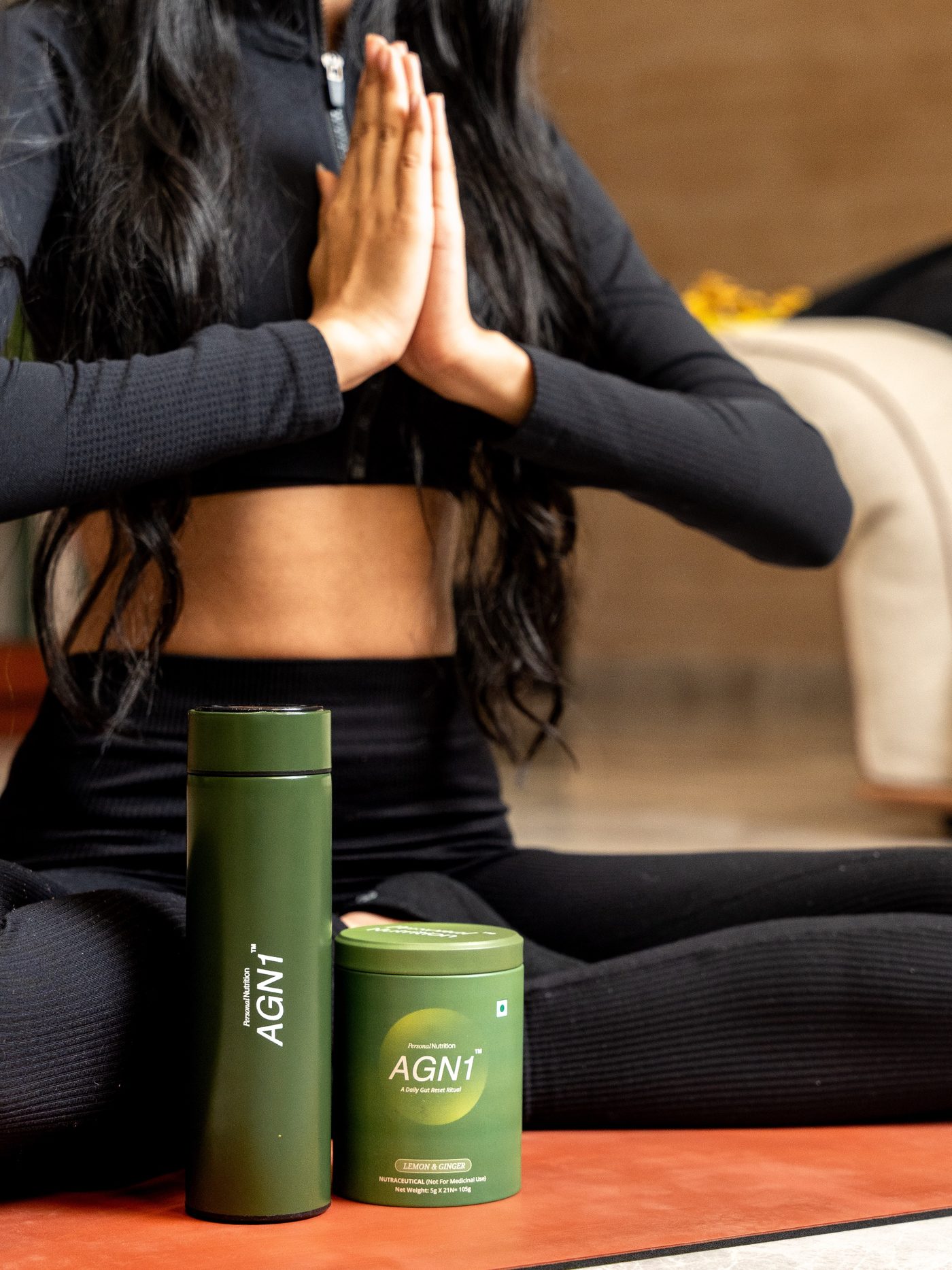 Woman seated in prayer pose beside an AGN1 flask and tub on a yoga mat