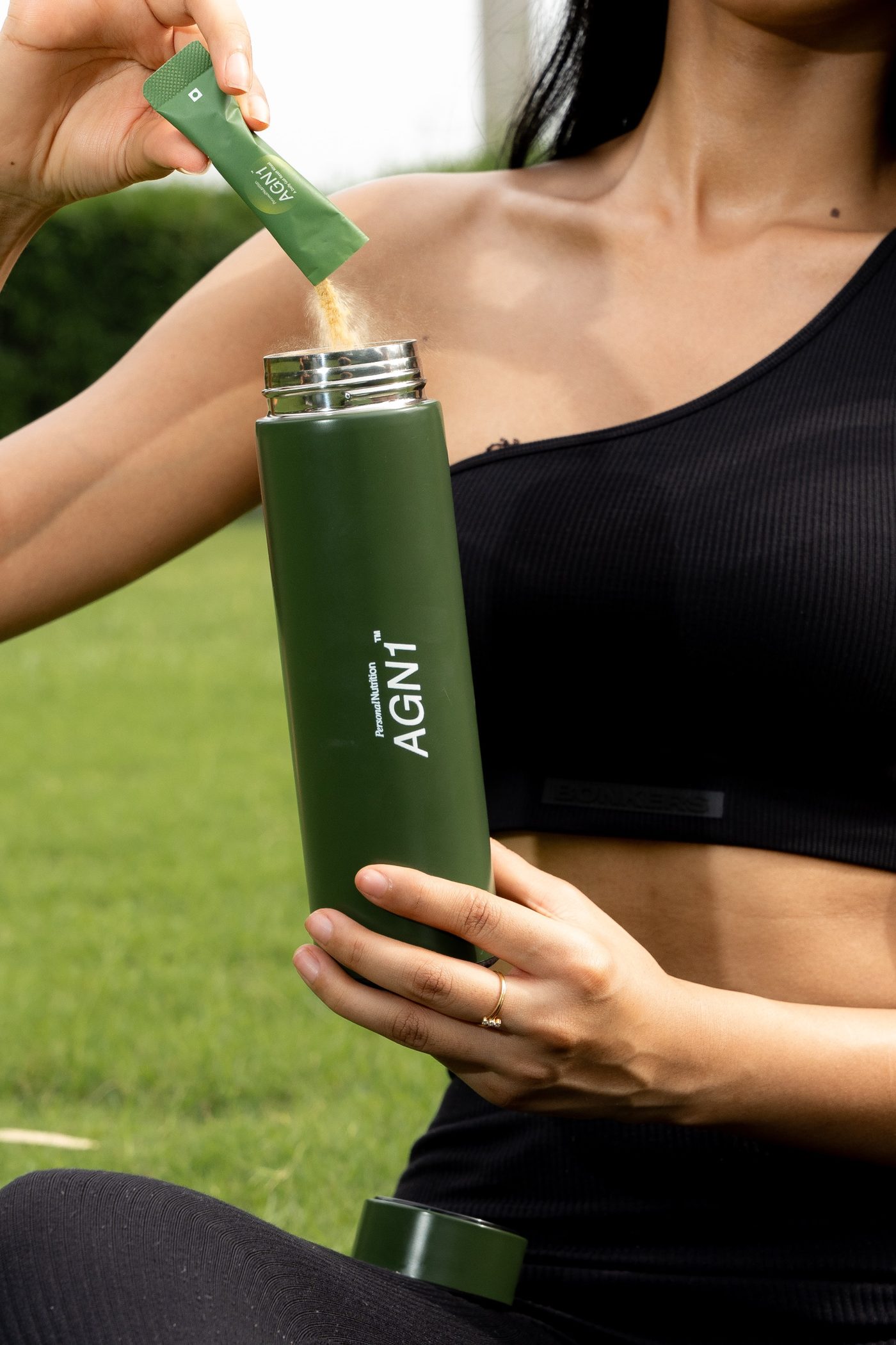 Woman pouring an AGN1 sachet into a green flask on a lawn