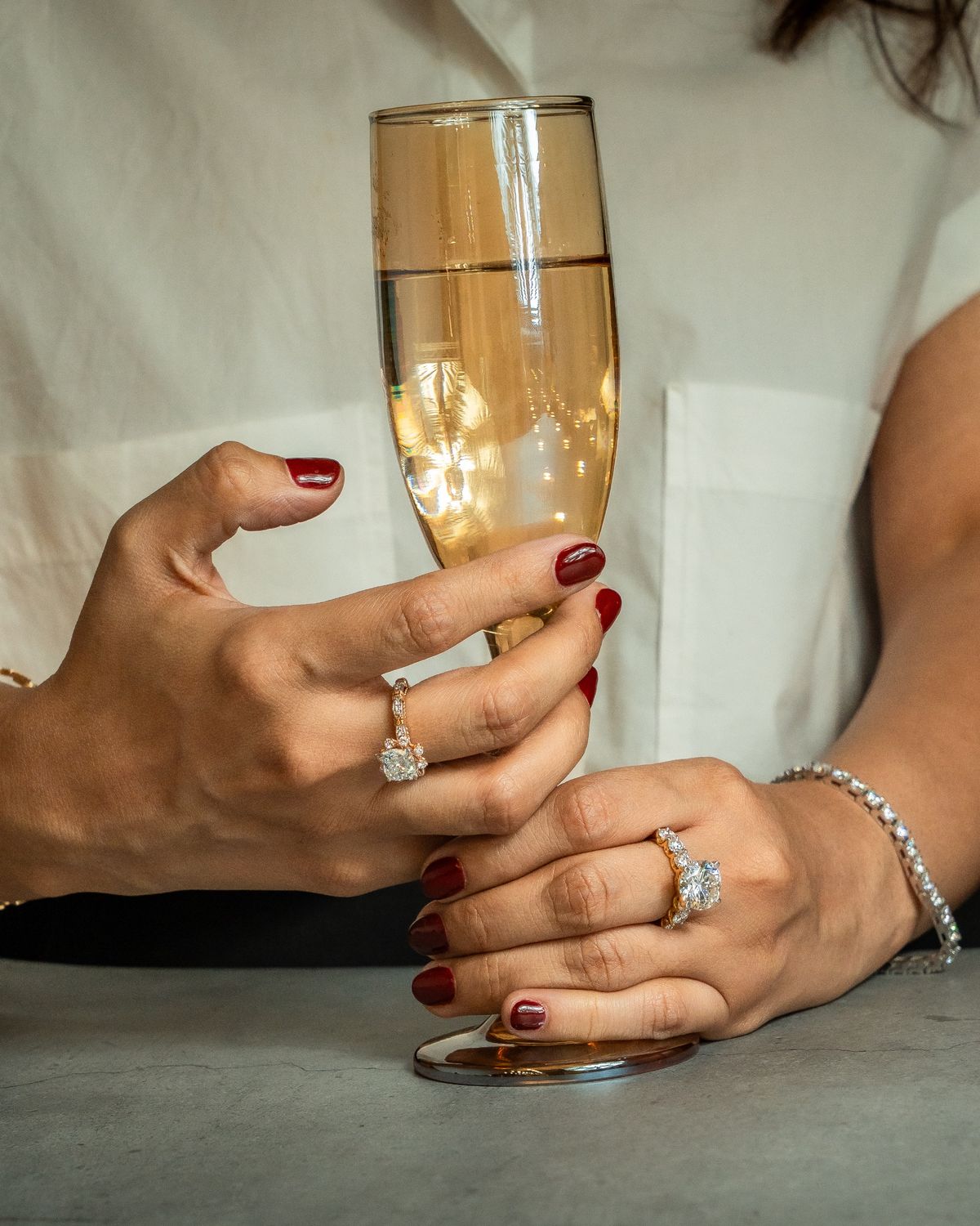 Hands holding a champagne flute, wearing diamond rings and a tennis bracelet