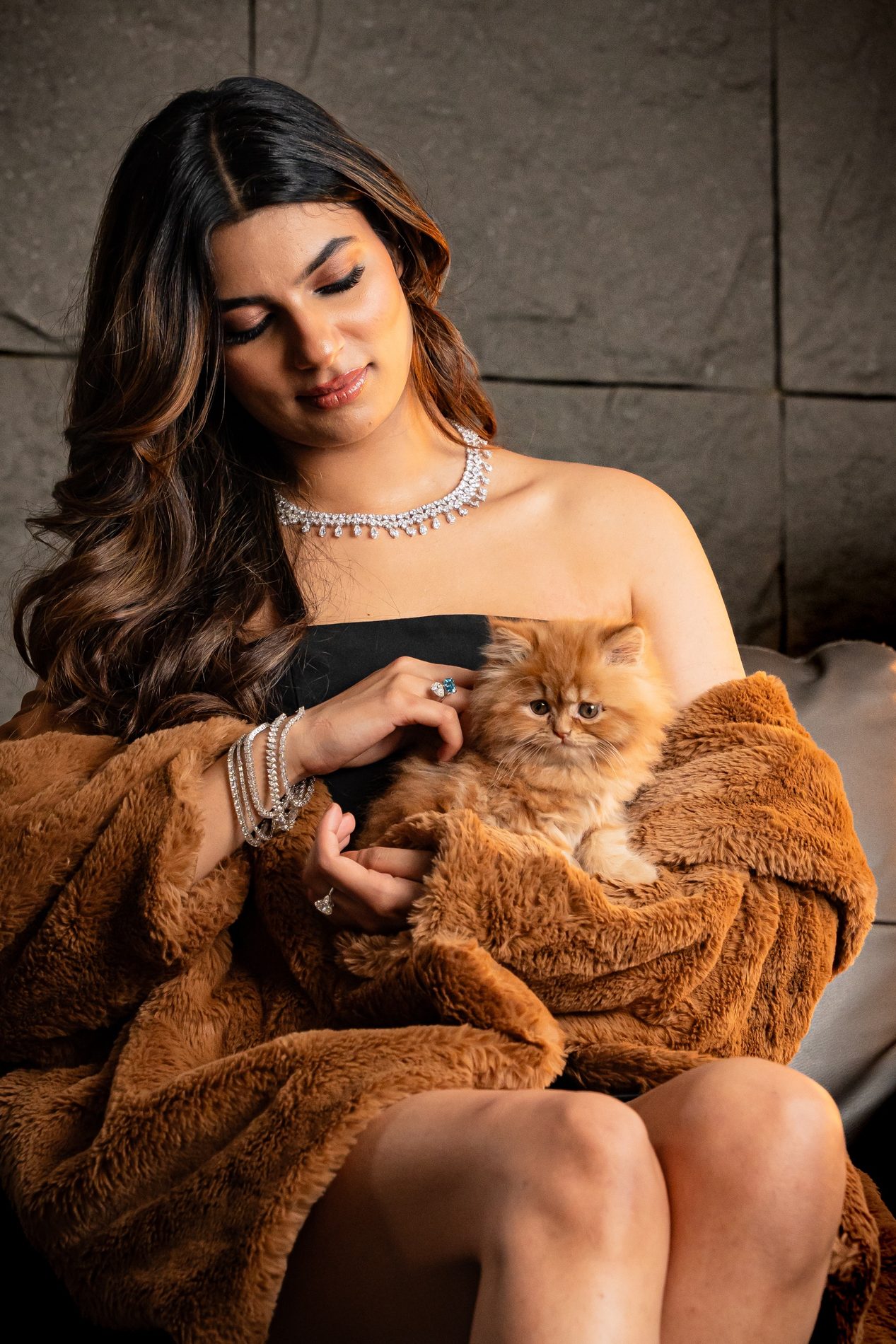 Seated woman in a fur coat with a kitten in her lap, wearing a diamond necklace