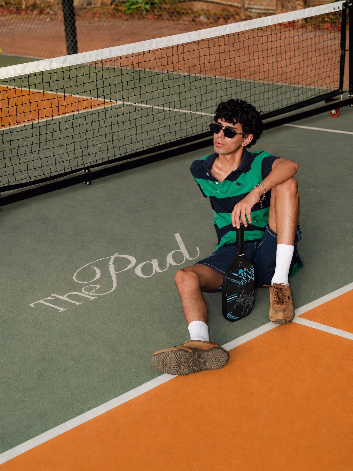 Man in a green striped polo seated on a court floor marked with The Pad lettering