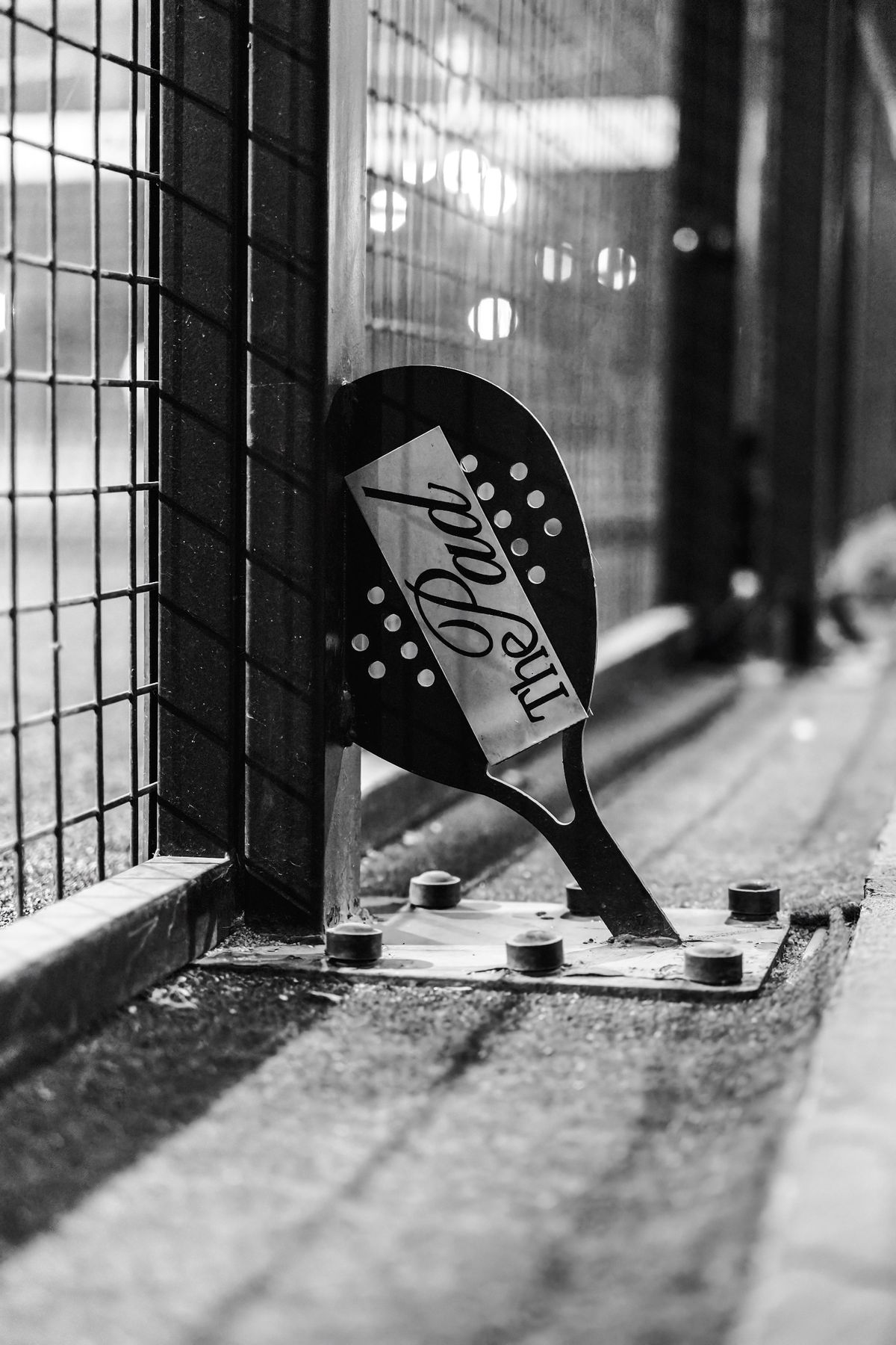 The Pad logo on a racket-shaped sign fixed to a court fence, in black and white